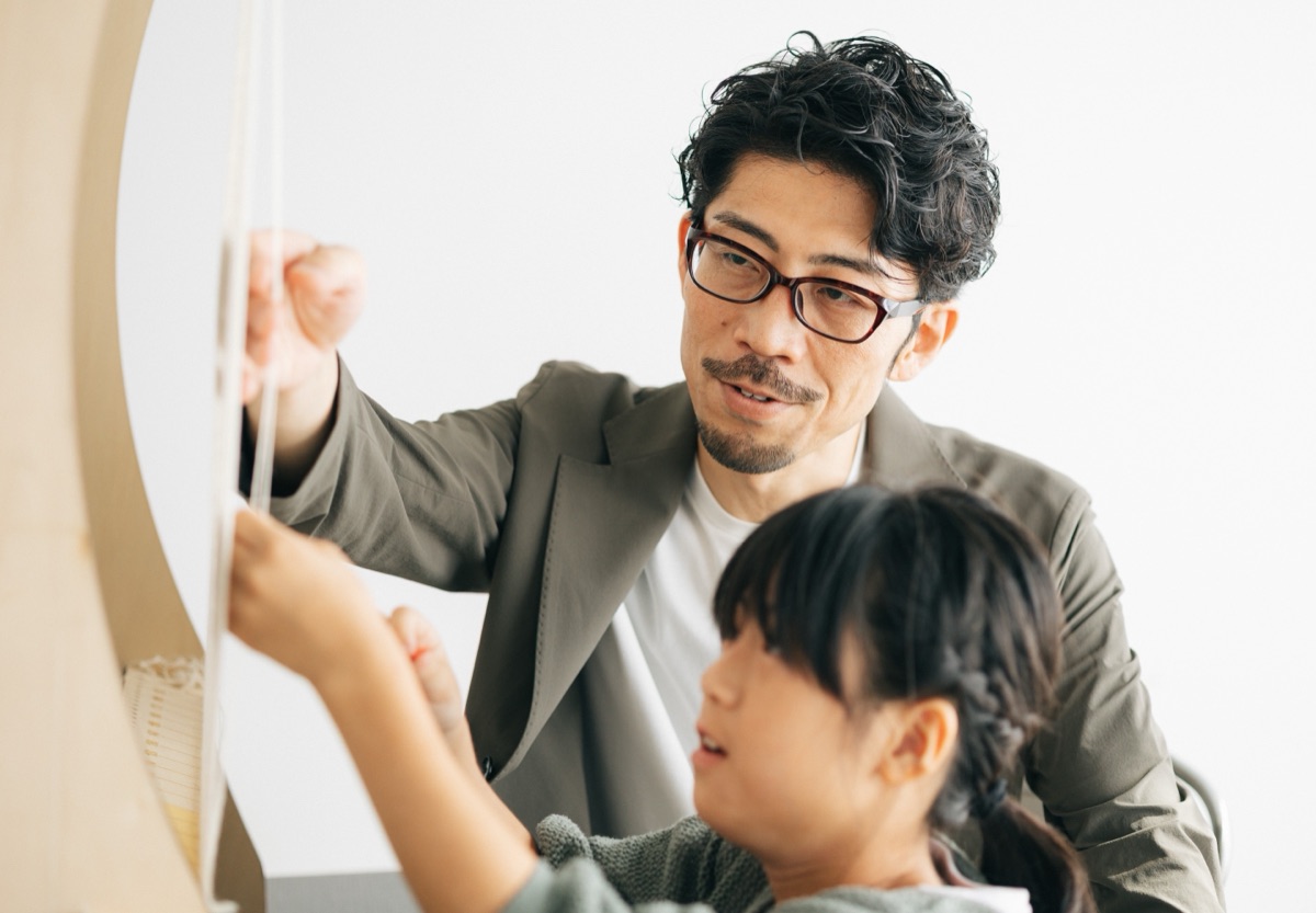 大人と子どもが並んで、張られた経糸に手を伸ばしている。