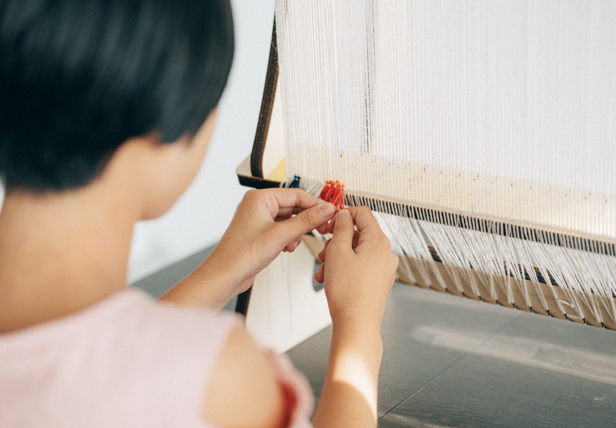子どもの手が、経糸のあいだにオレンジ色の糸を結んでいるところ。